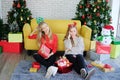 Caucasian couple girls friends sitting on the floor and holding big Gift boxes in Christmas party. They are drunk and bored.