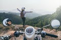 Caucasian couple riding motorcycle in Laotian mountains. Woman stands on cliff edge, hands up. Nong Khiaw village, Laos Royalty Free Stock Photo