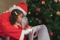 Caucasian cute child girl writing a letter with Santa Claus near a festively decorated Christmas tree. Father wear Santa Claus Royalty Free Stock Photo