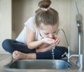 Caucasian cute girl is drinking from water tap or faucet in kitchen at home. Hydration. Lifestyle. Healthcare, healthy drink