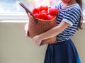 Caucasian cute girl in navy blue striped dress, carrying red hearts basket to cheer up family. Her grin shows happiness, warmth, c