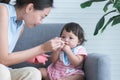 Caucasian Cute 7 month newborn baby girl deny eating blend mashed food, young Asian mother holding spoon feeding child, sitting on Royalty Free Stock Photo