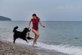 Happy owner of Bernese Mountain Dog on vacation on beach. Caucasian cute red haired woman in swimsuit runs around sea with her