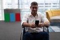 Caucasian disabled businessman using mobile phone while sitting on wheelchair in office