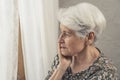 caucasian elderly pensioner lady depressed alone worried standing next to the window with white curtain