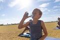 Caucasian elementary schoolboy drinking water while standing on field against bright sky