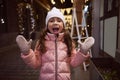 Emotional little girl smiles looking at camera, enjoying the Christmas atmosphere outdoors in the fairground at night