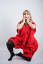 Caucasian emotive blonde girl in a huge plush suit of red strawberry on a white background in the Studio