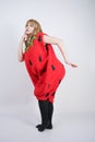 Caucasian emotive blonde girl in a huge plush suit of red strawberry on a white background in the Studio