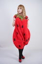 Caucasian emotive blonde girl in a huge plush suit of red strawberry on a white background in the Studio