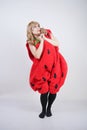 Caucasian emotive blonde girl in a huge plush suit of red strawberry on a white background in the Studio