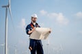 Caucasian engineer or technician man stand with holding drawiing paper and look to the paper and stand in front of windmill or Royalty Free Stock Photo