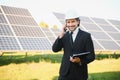 Caucasian engineer using smartphone while standing with solar panel at the background. Concept of alternative