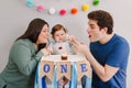 Caucasian family with baby boy celebrating his first birthday at home. Mother father dad with child kid toddler blowing candle on