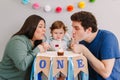 Caucasian family with baby boy celebrating his first birthday at home. Mother father dad with child kid toddler blowing candle on