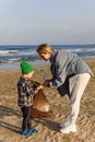 Caucasian family is collecting plastic waste on beach. Mother is teaching her son to help keep nature clean Royalty Free Stock Photo