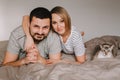 Caucasian family man and woman lying on bed in bedroom at home with oriental cat. Proud smiling pet owners with a domestic animal