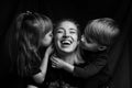 Caucasian Family Portrait in Black and White. mom daughter and son. mom laugh. son and daughter kiss mom on the cheeks Royalty Free Stock Photo