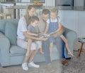 Caucasian family reading a book together on the couch at home. Mother and father teaching their little son and daughter Royalty Free Stock Photo