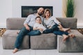 Caucasian family is sitting on a gray sofa at home cuddling up and looking at the camera. Father hugs his wife and son Royalty Free Stock Photo