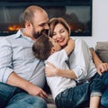 Caucasian family is sitting on a gray sofa at home cuddling up and looking at the camera. Father hugs his wife and son Royalty Free Stock Photo