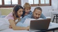 Caucasian family of three using laptop while lying on bed together, browsing internet or watching movie Royalty Free Stock Photo