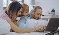 Caucasian family of three using laptop while lying on bed together, browsing internet or watching movie Royalty Free Stock Photo