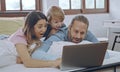 Caucasian family of three using laptop while lying on bed together, browsing internet or watching movie Royalty Free Stock Photo