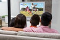 Caucasian family watching tv with football match on screen