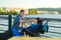 Father feeding disabled son in wheelchair hamburger by urban lake