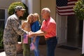 Caucasian father and military son shaking hands with mother and wife standing at house entrance