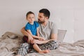 Caucasian father talking to boy son. Man parent hugs kid child on bed in a bedroom at home. Authentic lifestyle real family candid Royalty Free Stock Photo