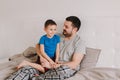 Caucasian father talking to boy son. Man parent hugs kid child on bed in bedroom at home. Authentic lifestyle real family candid Royalty Free Stock Photo