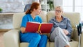 Caucasian female assistant in nursing home reading a book to an elderly retired woman Royalty Free Stock Photo