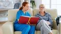 Caucasian female assistant in nursing home reading a book to an elderly retired woman Royalty Free Stock Photo