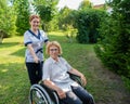 Caucasian female doctor walks with an elderly patient in a wheelchair in the park. Nurse accompanies an old woman on a