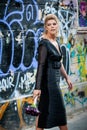 FASHION. Elegant blonde lady in front of a wall with graffiti. A wall vandalized with street graffiti art.