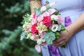 Caucasian female guest or bridesmaid wearing a lilac summer dress which shows a lovely baby bump and holding a wedding bouquet Royalty Free Stock Photo