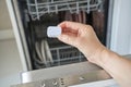 Caucasian female hand holding dishwasher tablet in kitchen with open dishwasher Royalty Free Stock Photo