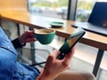 Caucasian female holding in hands cup of coffee and mobile phone having coffee break in restaurant. Morning coffee Royalty Free Stock Photo