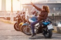 Caucasian female motorcyclist sitting on motorbike and getting a selfie with mobile phone