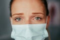 Caucasian female nurse trainee standing in doctors office wearing mask