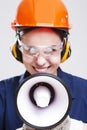 Caucasian Female Shouting Worker Posing with Megaphone In Front of Face and Wearing Hardhat for Protection. Focus on Megaphone Royalty Free Stock Photo