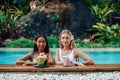 Caucasian female traveller with asian woman in pool with natural juice Royalty Free Stock Photo