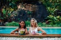 Caucasian female traveller with asian woman in pool with natural juice Royalty Free Stock Photo