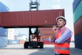 Caucasian foreman man is using walkie talkie to command his workers with crane lifting container in background in container depot