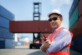 Caucasian foreman man is using walkie talkie to command his workers with crane lifting container in background in container depot