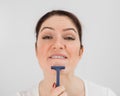 Caucasian funny woman shaves her face with a straight razor on a white background. Copy space. Royalty Free Stock Photo