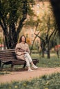 A Caucasian girl in a beige coat and blue jeans sits on a bench in a park in autumn and reads a book Royalty Free Stock Photo