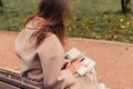 A Caucasian girl in a beige coat and blue jeans sits on a bench in a park in autumn and reads a book Royalty Free Stock Photo